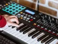 Hand spielt auf einem Keyboard, das für die Erzeugung von Synth-Musik verwendet wird. Viele Knöpfe und Pads sind sichtbar.