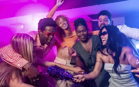 Fröhliche Freunde tanzen ausgelassen zu ihrer **dance music playlist** im Club, umgeben von lila und blauer Beleuchtung.