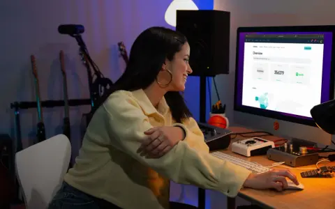 Junge Frau am Computer, die Statistiken für digitalen Musikvertrieb prüft. Gitarren im Hintergrund.