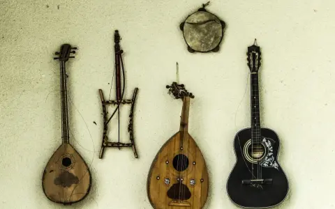 Verschiedene Saiteninstrumente und ein Tamburin hängen an der Wand. Seit wann gibt es Gitarren? Die Geschichte der Gitarre reicht weit zurück.