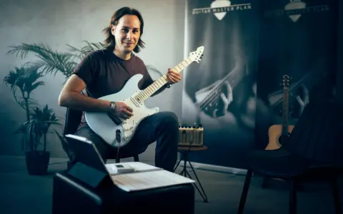 Mann mit E-Gitarre, bereit, online Gitarre zu lernen. Noten und Tablet liegen bereit.