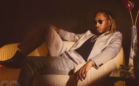 Ein Hip-Hop-Künstler in einem schicken Anzug entspannt sich auf einem Sofa, trägt Sonnenbrille und Schmuck.