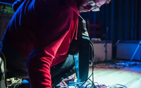 Musiker mit roten Kapuzenpullover beugt sich über ein Pedalboard, um den "Delay"-Effekt einzustellen.