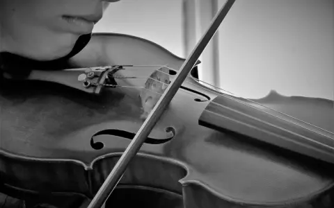 Nahaufnahme einer Person, die eine Geige spielt. Der Bogen streicht über die Saiten und erzeugt die Klänge bester klassischer Musik.