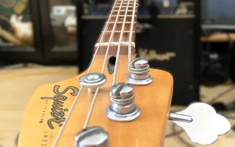 Nahaufnahme des Bass-Kopfes mit Saiten und Stimmmechaniken. Der Schriftzug "Squier by Fender Jazz Bass" ist sichtbar. Perfekt, um den Bass einzustellen.