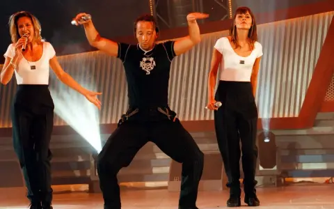 Drei Künstler in Schwarz-Weiß-Outfits performen auf einer Bühne. Die Frau links singt, der Mann in der Mitte tanzt, die Frau rechts hält ein Mikrofon. Ein energiegeladener Moment für **dance & electronic** Musik.
