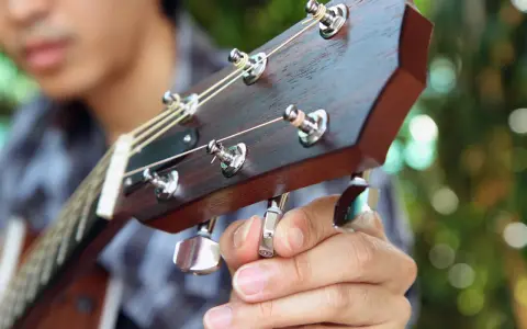 Nahaufnahme: Eine Hand stimmt eine 12-saitige Gitarre. Die Saiten sind gespannt, die Mechaniken glänzen.