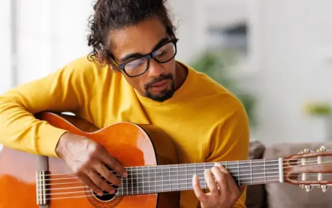 Mann mit Brille hält eine Gitarre und spielt darauf.