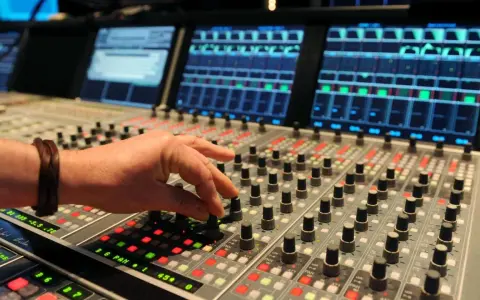 Hand am Mischpult, das an die Erfindung von Autotune erinnert. Tontechniker regelt Regler.