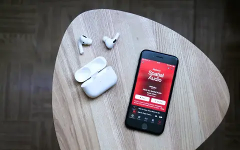 iPhone mit Apple Music Update zeigt "Made for Spatial Audio". AirPods und Ladecase liegen daneben.