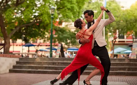 Ein Paar tanzt leidenschaftlich Tango. Die Frau trägt ein rotes Kleid, der Mann einen Anzug. Ein klassischer Tanzgenre-Moment.