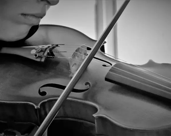 Nahaufnahme einer Person, die eine Geige spielt. Der Bogen streicht über die Saiten und erzeugt die Klänge bester klassischer Musik.