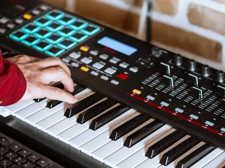 Hand spielt auf einem Keyboard, das für die Erzeugung von Synth-Musik verwendet wird. Viele Knöpfe und Pads sind sichtbar.