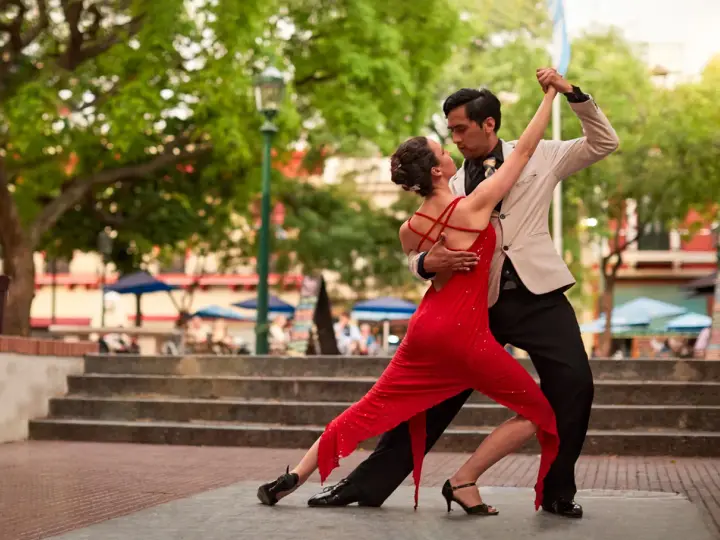 Ein Paar tanzt leidenschaftlich Tango. Die Frau trägt ein rotes Kleid, der Mann einen Anzug. Ein klassischer Tanzgenre-Moment.