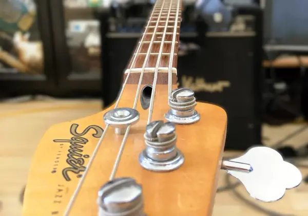 Nahaufnahme des Bass-Kopfes mit Saiten und Stimmmechaniken. Der Schriftzug "Squier by Fender Jazz Bass" ist sichtbar. Perfekt, um den Bass einzustellen.