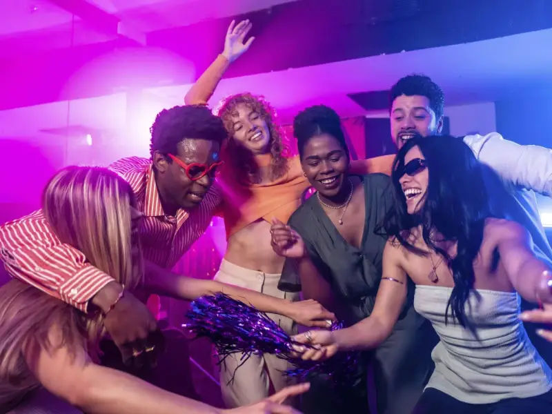 Fröhliche Freunde tanzen ausgelassen zu ihrer **dance music playlist** im Club, umgeben von lila und blauer Beleuchtung.