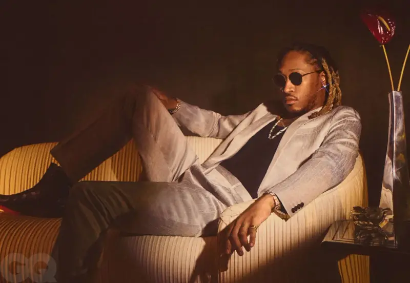 Ein Hip-Hop-Künstler in einem schicken Anzug entspannt sich auf einem Sofa, trägt Sonnenbrille und Schmuck.